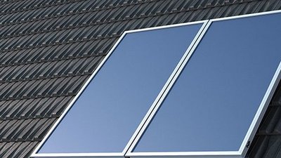 Zwei große Solarpanels sind auf einem schrägen Dach montiert, unter einem klaren blauen Himmel.