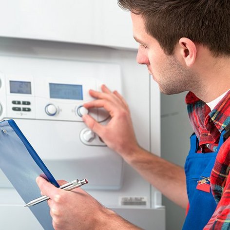 Ein Anlagenmechaniker mit einem Klemmbrett dreht an einer Heizungsanlage