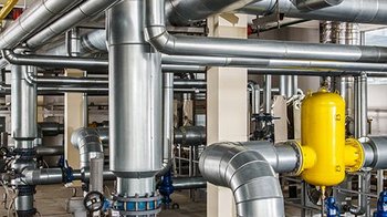 Ein komplexes Netzwerk aus glänzenden Metallrohren und Ventilen, das in einer industriellen Umgebung angeordnet ist.