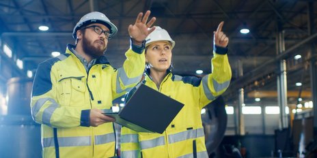 Ein Mann und eine Frau die einen Bauhelm und eine Warnjacke tragen 